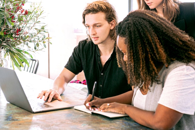 Man reviewing CRM reports on laptop with woman taking notes